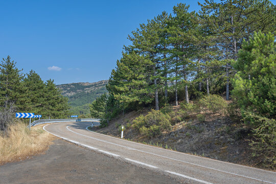 High-mountain road with protective metal railings and sweeping curves revealing panoramic views of snow-capped peaks in the background