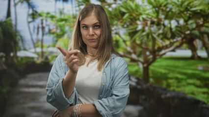 Woman points finger to self in forest path, outdoors green park setting with stern expression; personal denial.