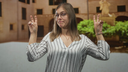 Young blonde woman smirking and making air quotes gesture with fingers in a historic old town...