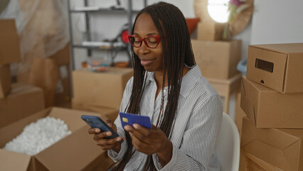Woman unpacking in new home surrounded by boxes using smartphone and credit card indicates a fresh start in an urban living room setting with modern interior design