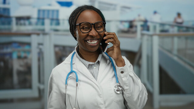 Female doctor talking on a smartphone at a seaside port with boats in the background, showcasing a blend of professional and leisurely outdoor setting.