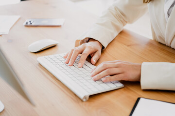 Professional businesswoman typing on a white keyboard in a modern office environment with elegant formalwear