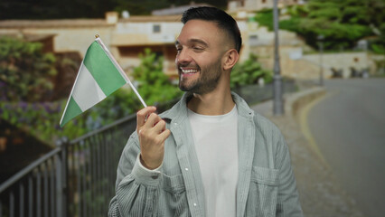 Young man smiling outdoors holding nigeria flag on urban city street expressing happiness with vibrant backdrop.