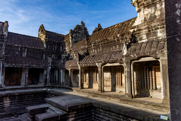 Fototapeta premium Ancient inner courtyard of angkor wat temple in siem reap, cambodia, featuring stone columns, carved bas-reliefs and a ritual bath in warm morning light