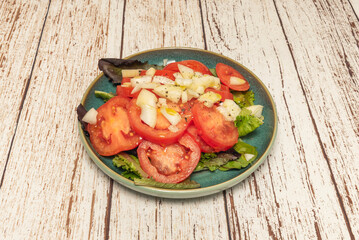 Salad preparation where thickly sliced ​​tomatoes are intertwined with white onion rings on a bed of crisp iceberg lettuce
