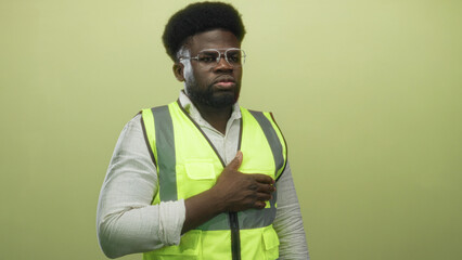 Man wearing safety glasses and reflective neon vest holding hand over chest against green studio...