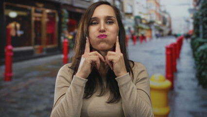 Fototapeta premium Woman outdoors on street gesturing with cheeky expression surrounded by vibrant urban scenery and red posts.