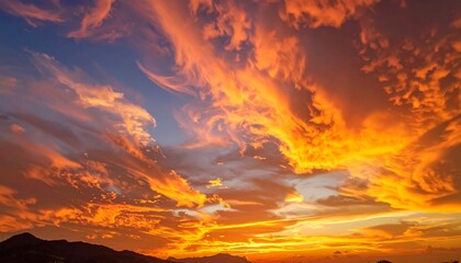 Fiery, dynamic orange and blue sunset over distant mountains, showcasing dramatic cloud formations in a colorful sky