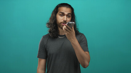 Man tapping smartphone screen with fingers in studio against teal wall; concentration communication.