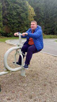 Young overweight man exercising on outdoor machine