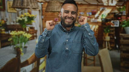 Fototapeta premium Man smiling with clenched fists beside yellow tulip bouquets in a rustic flower shop set in a studio building interior; joy.