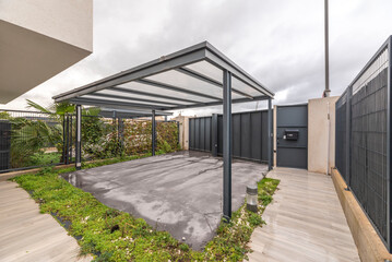 Obraz premium Open carport with a dark green painted metal frame and a sloping tiled roof.