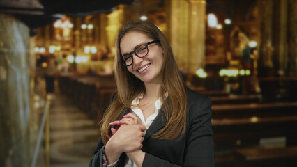 Young caucasian woman wearing glasses smiling gently with hands on chest in a historic building;...