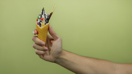 Caucasian man holding ice cream cone against a yellow background, showcasing colorful toppings and...