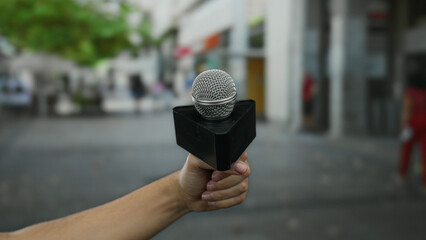 Caucasian man holding microphone on city street in outdoor urban setting, capturing media,...