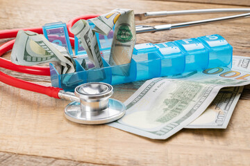 One-hundred-dollar bills stuffed into a blue pill organizer, representing the high cost of medicine in the United States.