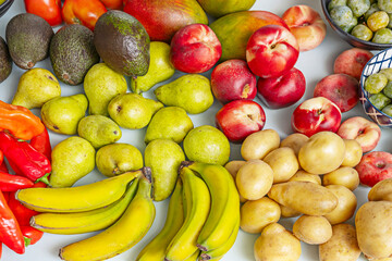 Still life photography of bananas, pears, avocados, potatoes, nectarines, and figs showing different stages of ripeness on a uniform pastel blue background