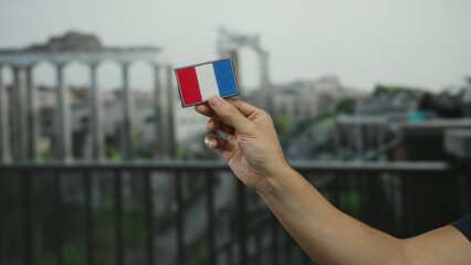 Man holding a french flag patch with ancient roman ruins in the background on a city street.