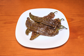 Side dish of fried green peppers with garlic shoots, elegantly arranged on a white plate that enhances their golden green color and crunchy texture
