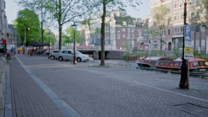 Blurry scene of amsterdam street with defocused bokeh capturing a serene canal, parked cars, trees,...