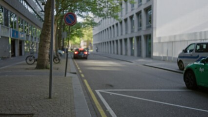 Urban street view captured with a blurry focus showing cars and buildings in a european city, emphasizing modern architecture and serene atmosphere on a sunny day.