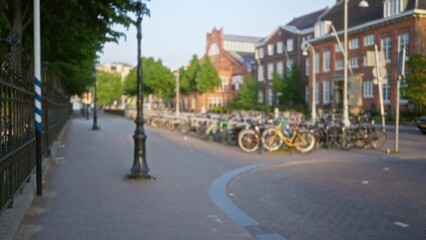 Blurred bicycles line the street in a tranquil european city with historic architecture, creating a defocused urban scene under clear skies.