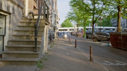 Blurred view of european city street with bicycles parked near a staircase and trees lining the road, capturing the essence of urban life through defocused perspectives.