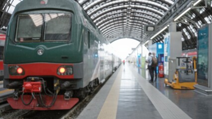 Train on an empty platform beneath an arched station canopy, locomotive foreground with tracks and signage, soft defocused bokeh at station; background copyspace.