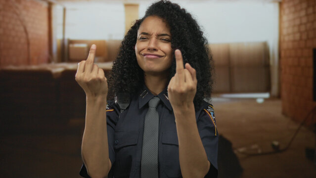 Woman police officer flips middle finger while smiling inside unfinished building; bold attitude defiance.
