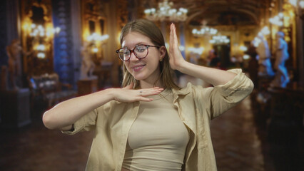 Young blonde woman frames face with hands amid sculpture exhibits at museum gallery; joy discovery wonder curiosity.