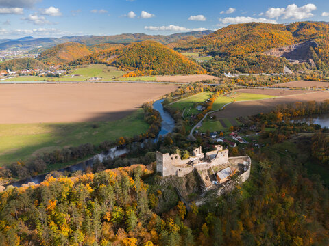 Aerial view of the ruins of Reviste Castle perched atop a hill, embraced by autumn's golden hues and a winding river, Zarnovica, Slovakia.