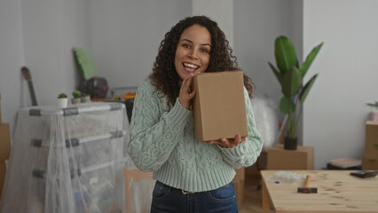 Young woman in new home holding a cardboard box joyfully in a cozy living room with unpacked items...