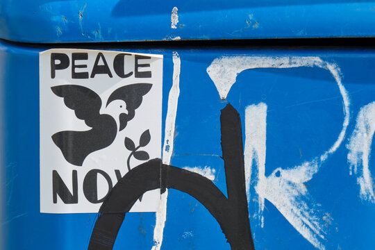 Sticker with a peace dove and the text peace now on a blue trash can with black and white graffiti