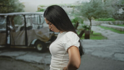 Fototapeta premium Woman holds lower back while standing on a paved street in an outdoor urban setting; backache discomfort.