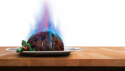A low view of a traditional Christmas pudding on a round plate with holly and blue flames of brandy on top of a wooden table isolated against a transparent background.