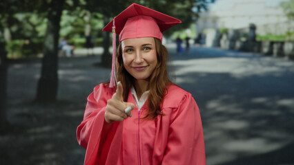Woman in graduation gown pointing with smile in city street celebrating academic success outside during daytime.