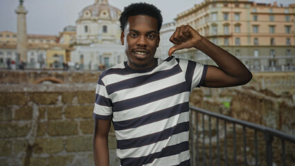 Fototapeta premium Man wearing striped shirt shows thumb down gesture at ancient building overlooking ruins; disapproval.