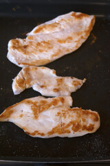grilled chicken breast slices cooking on hot griddle pan with utensils