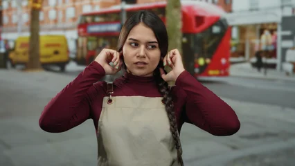 Fototapete Londoner Roter Bus Woman in apron with closed eyes covers her ears on bustling city street featuring iconic red bus and urban backdrop.  © Krakenimages.com