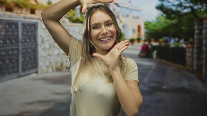 Fototapeta premium Woman smiling with hands framing face on urban street under blue sky showcasing happiness and confidence in a casual outdoor city setting.