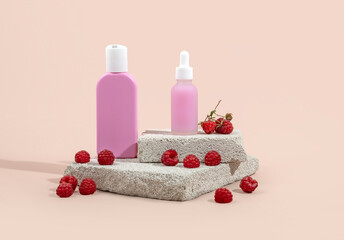 Pink bottles of cosmetics and raspberries on a stone podium on a beige background.