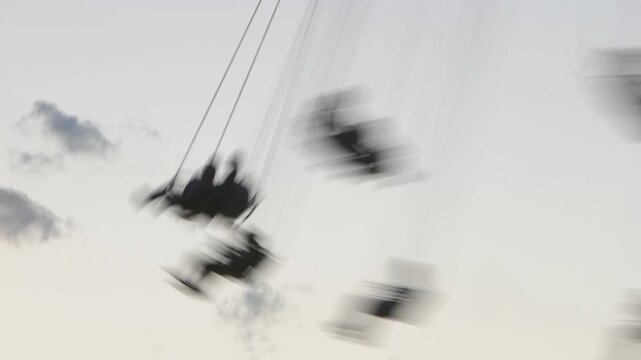 Abstract swing ride captured with low shutter speed, creating heavy motion blur against a pale sky. Dreamlike, surreal, and experimental imagery evoking freedom, speed, and disorientation.