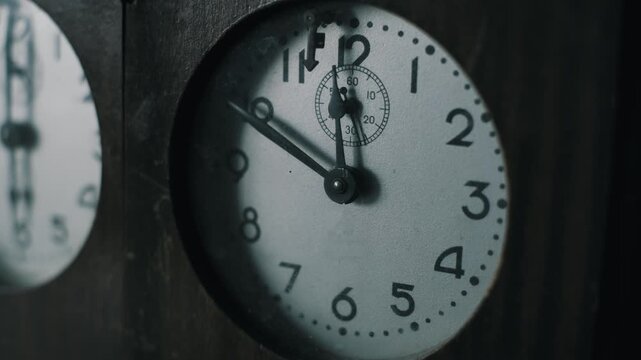 Angled shot of an antique clock with a dusty glass face. The second hand ticks as the minute hand approaches twelve, encased in dark wood with a worn texture for a historical or deadline concept.