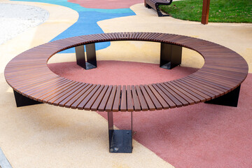 Circular wooden bench around playground element with colorful rubber coating, modern outdoor recreation area. Real photo. For landscape architecture, park design. Real photo