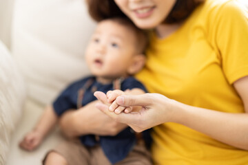 Loving asian mom carying of her newborn baby at home. Mother and baby boy playing in sunny bedroom. Parent and little kid relaxing at home. Family having fun together. Childcare, maternity concept.