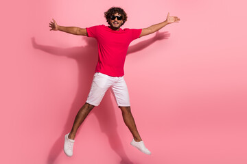 Energetic young man in a bright casual outfit joyfully jumping with arms outstretched against a pastel pink background