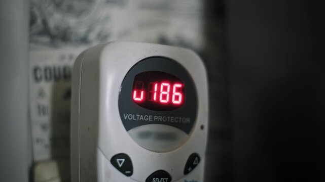 Close-up of a digital voltage protector showing low and fluctuating power. The red LED display indicates an unstable current around 185 volts before the safety device cuts power.