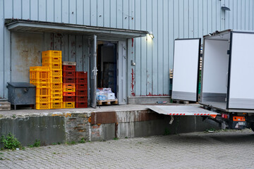 Loading dock of an industrial building with stacked plastic crates, open delivery truck, and pallets near the entrance.