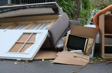 Discarded furniture and household items on the street, including a door, sofa, microwave, and cardboard boxes.
