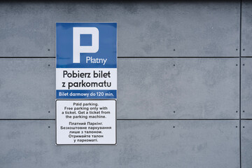 Paid parking instruction sign on a gray wall with text in Polish, English, and Ukrainian.